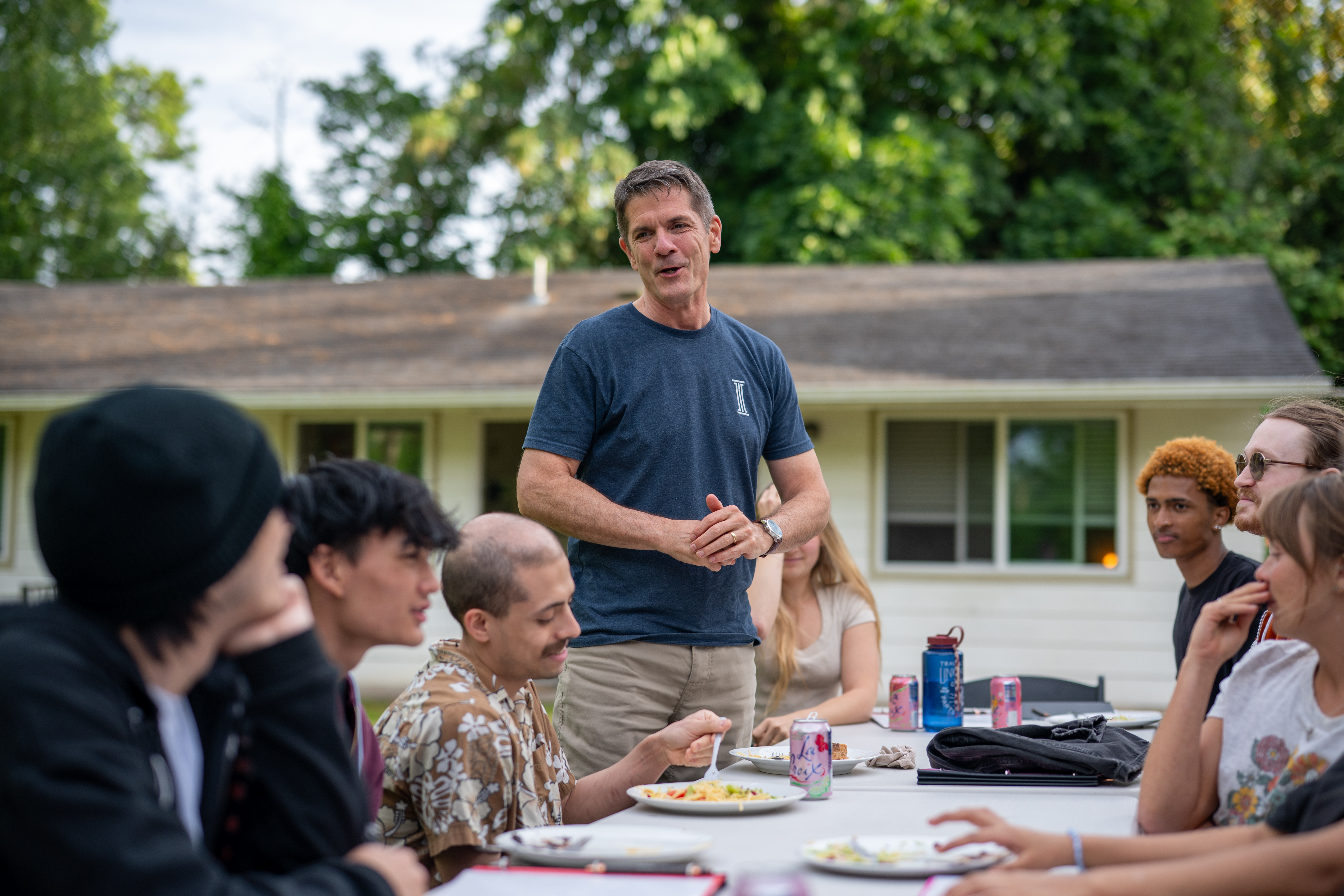 A mentor speaking with young people gathered around a shared outdoor meal