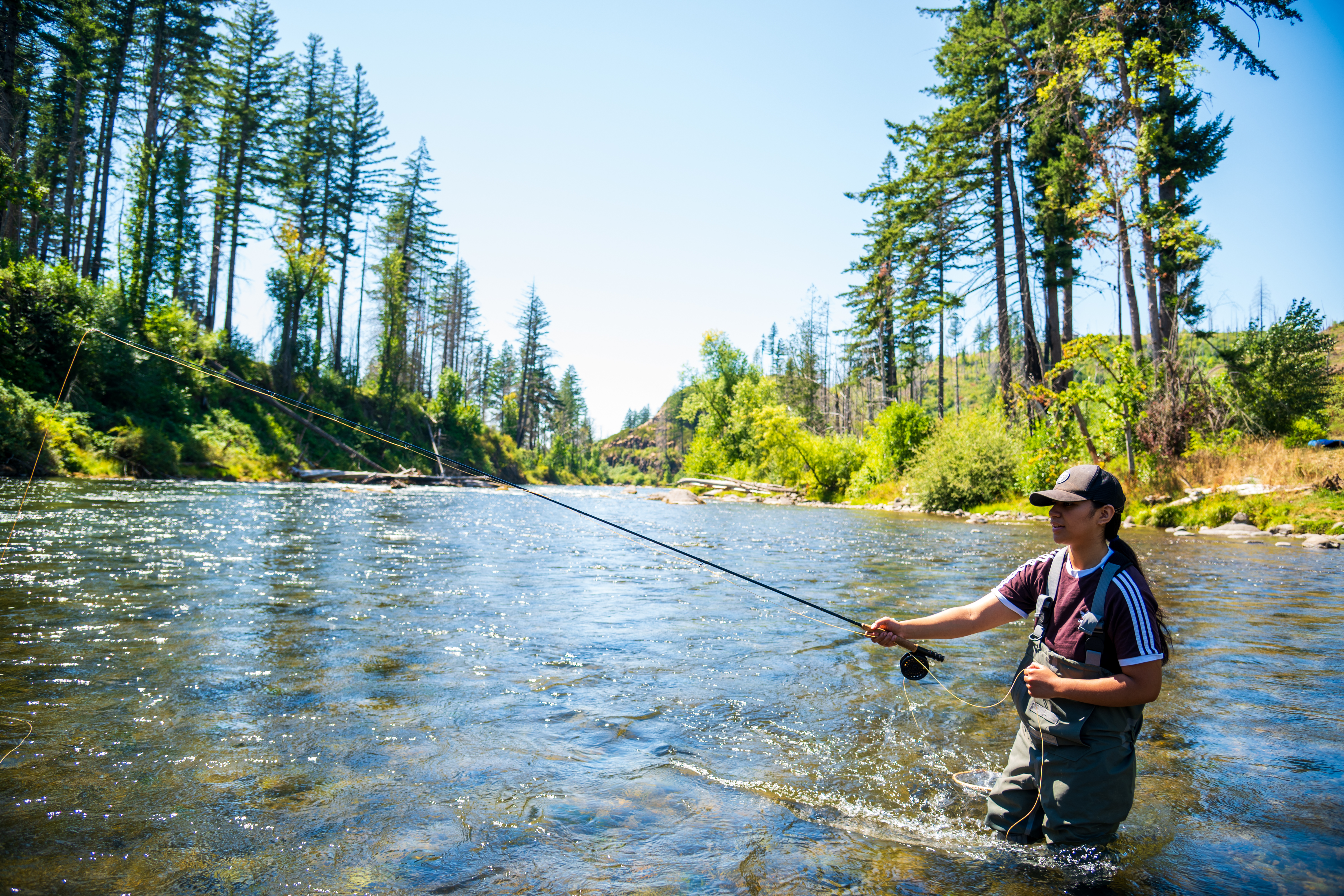 A young person learning to fly fish in a forest river